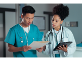 A doctor stands with a nurse looking at paperwork in a file.